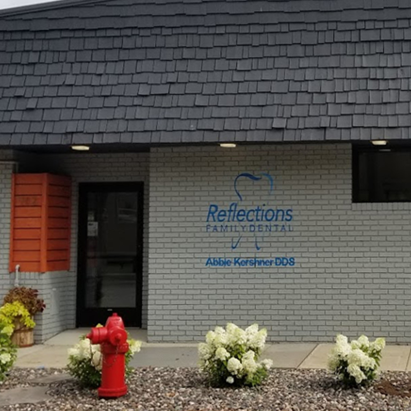 Image description: the exterior of the Reflections Family Dental office in Willmar, Minnesota. The building is blue painted bricks and has the dental logo painted on the front.